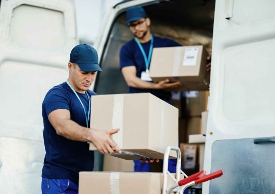 young-courier-his-colleague-unloading-cardboard-boxes-from-delivery-van_11zon