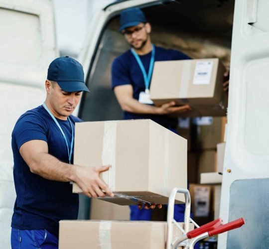 young-courier-his-colleague-unloading-cardboard-boxes-from-delivery-van_11zon